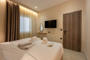 A hotel room with a bed, a television, a wooden door, and a window with curtains.
