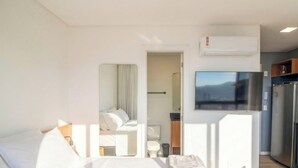 A hotel room with a bed, a TV mounted on the wall, a refrigerator, and a window with a view. - Studio in Condo w/ Pool in Blumenau Pin1906 (Blumenau)