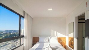 A hotel room with a bed, a window with curtains, a view of the city, and a door. - Studio in Condo w/ Pool in Blumenau Pin1906 (Blumenau)