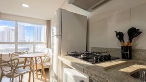 Eine moderne Küche mit Gasherd, Kühlschrank und Blick auf hohe Gebäude durch große Fenster.