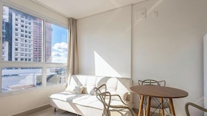 Ein modernes Zimmer mit einem weißen Sofa, einem runden Holztisch und einem großen Fenster mit Blick auf die Stadt.