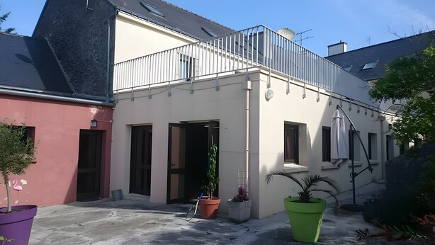 A building with a balcony, potted plants, and a clear sky.