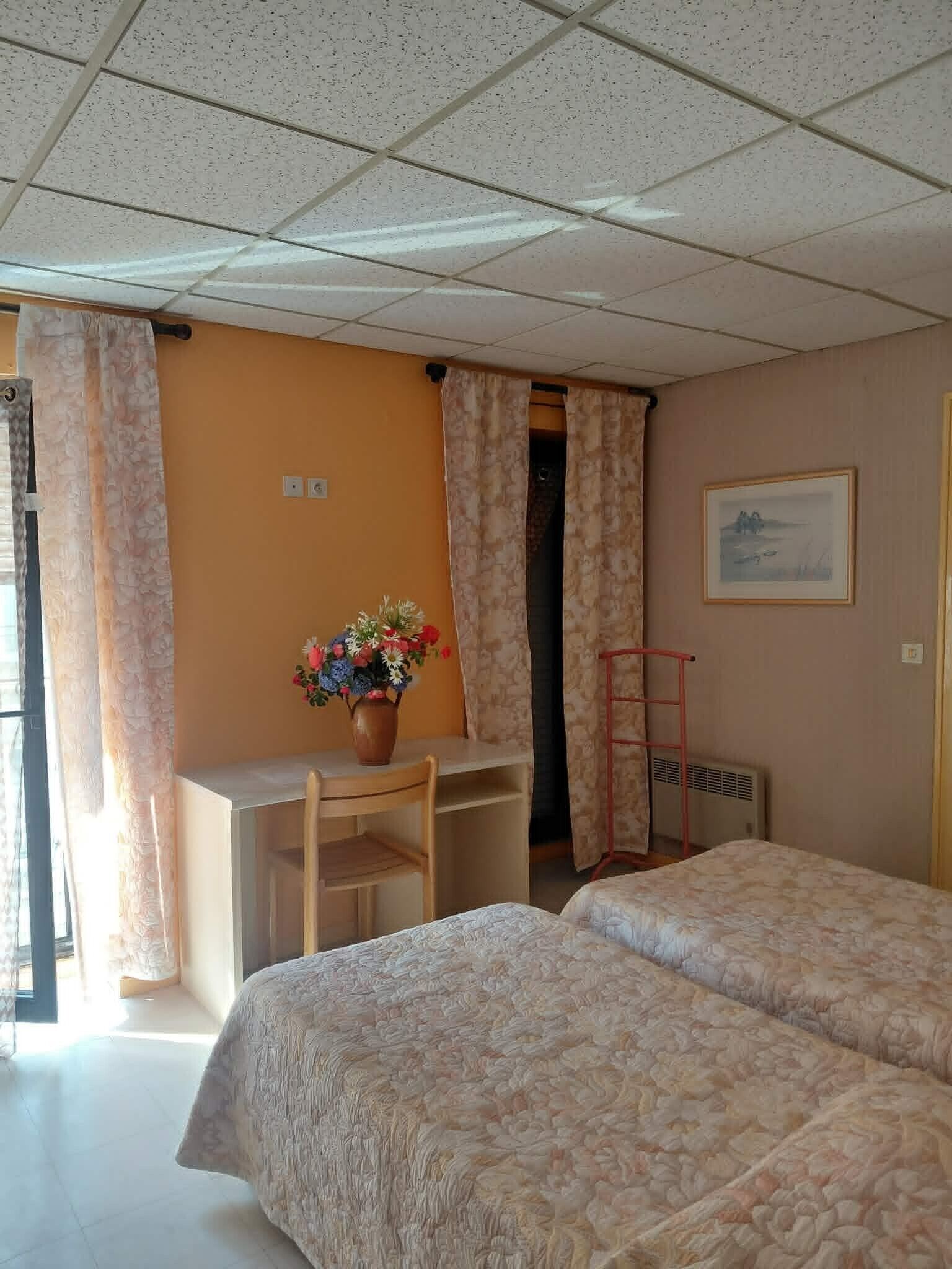 Een kamer met twee bedden, een bureau, een stoel, een raam met gordijnen en een radiator.