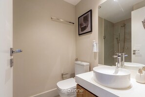 Ein modernes Badezimmer mit Toilette, Waschbecken, Dusche und einem großen Spiegel.