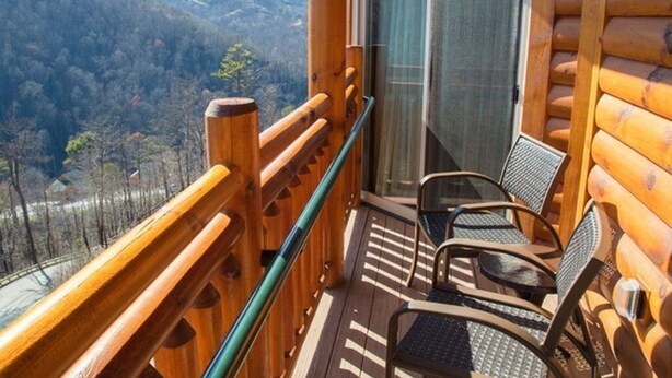 Un balcone con vista su una valle boscosa, una ringhiera di legno e due sedie.