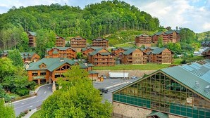 Un lodge con diversi edifici in legno, una struttura centrale in vetro e uno sfondo collinare boscoso.