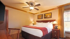 Una camera d'albergo con un letto, una sedia di legno, un comodino con una lampada e una ventola a soffitto.