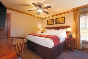 Ein Hotelzimmer mit einem Bett, einem Holzstuhl, einem Nachttisch mit Lampe und einem Deckenventilator.