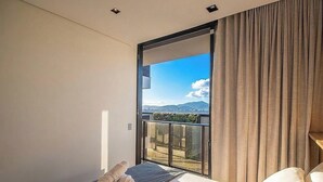Ein Schlafzimmer mit einer großen Schiebeglastür, die auf einen Balkon mit Blick auf die Stadt führt.