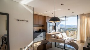 Eine moderne Küche mit einem großen Kühlschrank, ein Essbereich mit einer Couch und Stühlen sowie ein Blick auf die Stadt durch große Fenster.