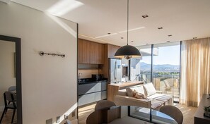 A modern kitchen with a large refrigerator, a dining area with a sofa and chairs, and a view of the city through large windows. - Condo Apt w/ Pool in Estados, Balneario Tso0314 (Balneário Camboriú)
