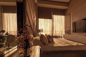 A hotel room with a bed, a bedside table with a vase of flowers, a mirror, and a large window with curtains. - Paradise Awaits | Ocean View Condo (Bucerías)