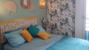 A bed with patterned bedding, a headboard with a decorative design, a wall-mounted fan, a wall lamp, and a floral wallpaper. - Port Fréjus: harbor view, spacious 1-bedroom apartment (47m²), air conditioning, swimming pool—for 4 lucky guests. (Fréjus)