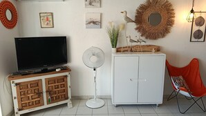 A room with a TV on a wooden cabinet, a white cabinet with a mirror, a fan, and a red chair. - Port Fréjus: harbor view, spacious 1-bedroom apartment (47m²), air conditioning, swimming pool—for 4 lucky guests. (Fréjus)