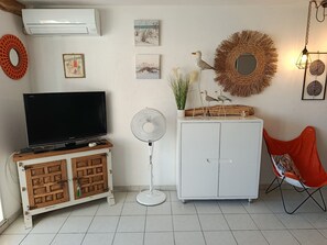 Ein Zimmer mit Fernseher auf einer Holzkommode, einer weißen Kommode mit Spiegel, einem Ventilator und einem roten Sessel.