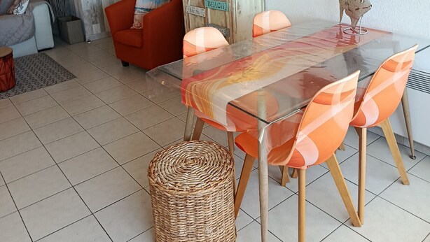 A dining area with a glass-top table, orange chairs, a wicker basket, and a red armchair. - Port Fréjus: harbor view, spacious 1-bedroom apartment (47m²), air conditioning, swimming pool—for 4 lucky guests. (Fréjus)