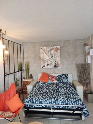 A bedroom with a bed, pillows, a side table, a chair, a wall art piece, and a hanging light fixture. - Port Fréjus: harbor view, spacious 1-bedroom apartment (47m²), air conditioning, swimming pool—for 4 lucky guests. (Fréjus)