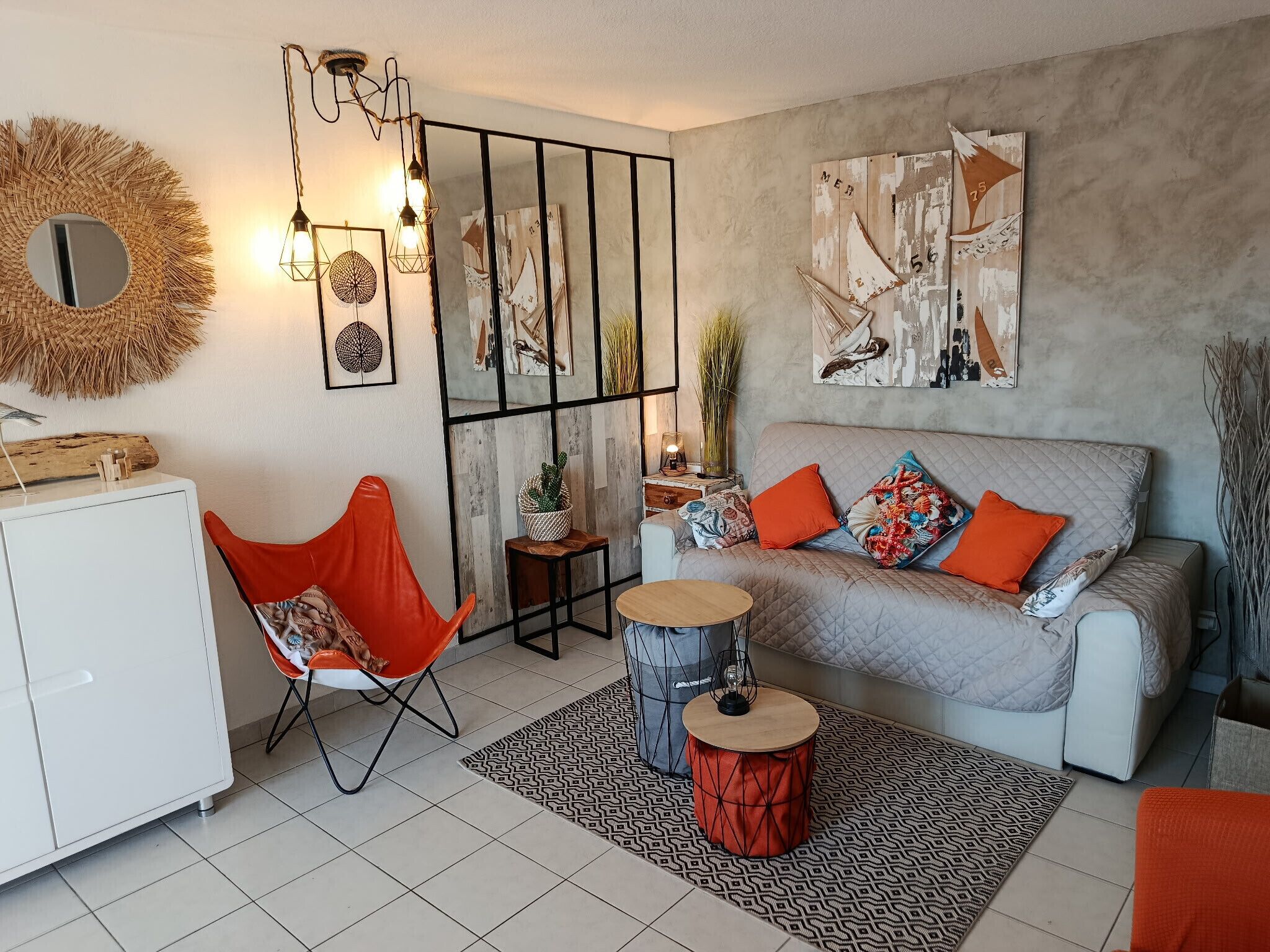 A modern living room with a sofa, a red chair, a round table, and a decorative mirror.