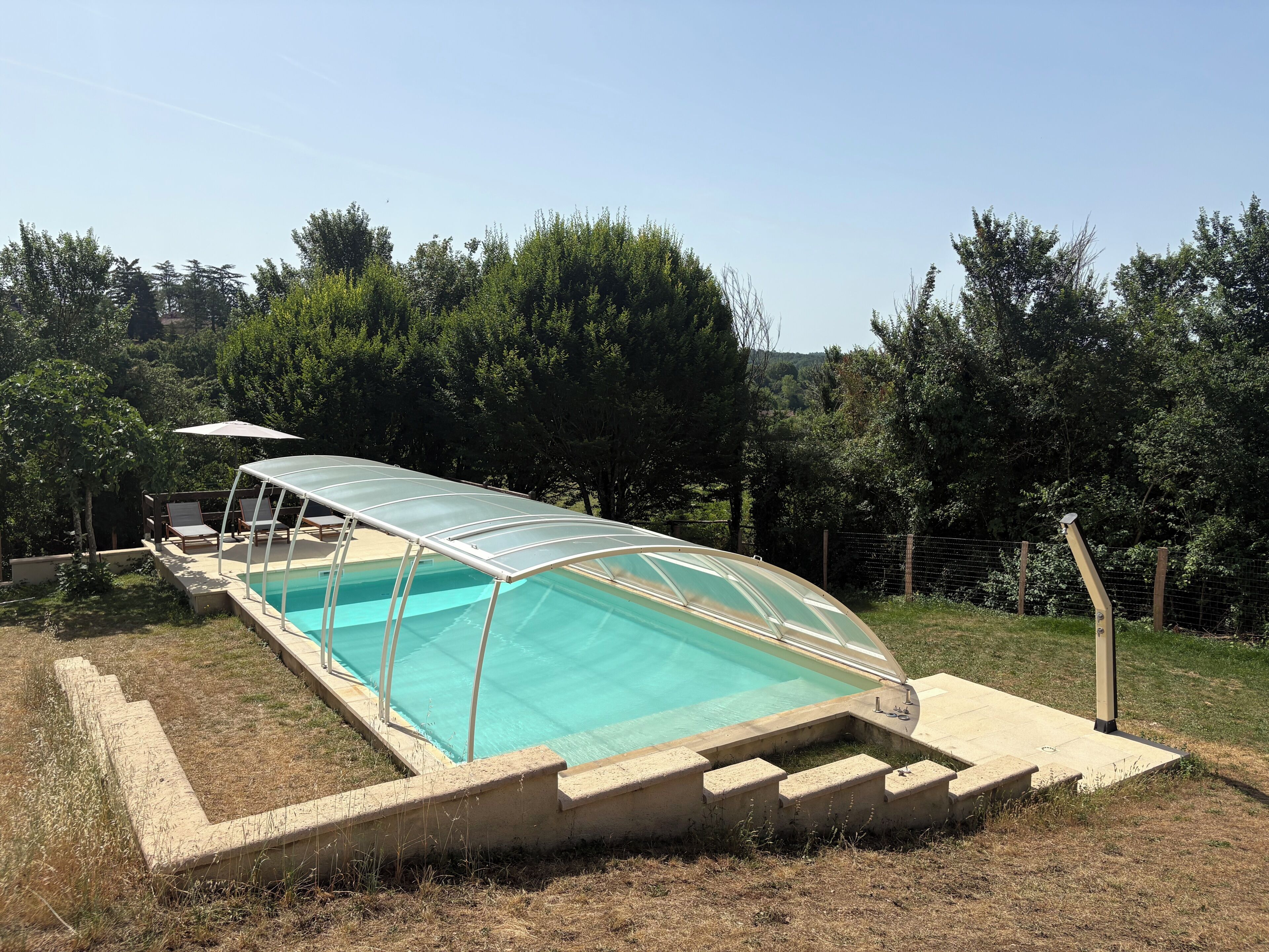 Une piscine dotée d’une enceinte en verre, entourée d’une terrasse en béton et d’une zone herbeuse.