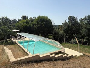 A swimming pool with a glass enclosure, surrounded by a concrete deck and a grassy area. - Périgord-style house for 6 people with a pool, in a quiet location with a large garden, 10 minutes from Monpazier (Marsalès)