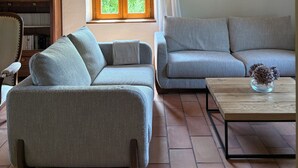 Olohuoneessa on kaksi sohvaa, sohvapöytä, kirjahylly ja ikkuna, jossa on verhot.