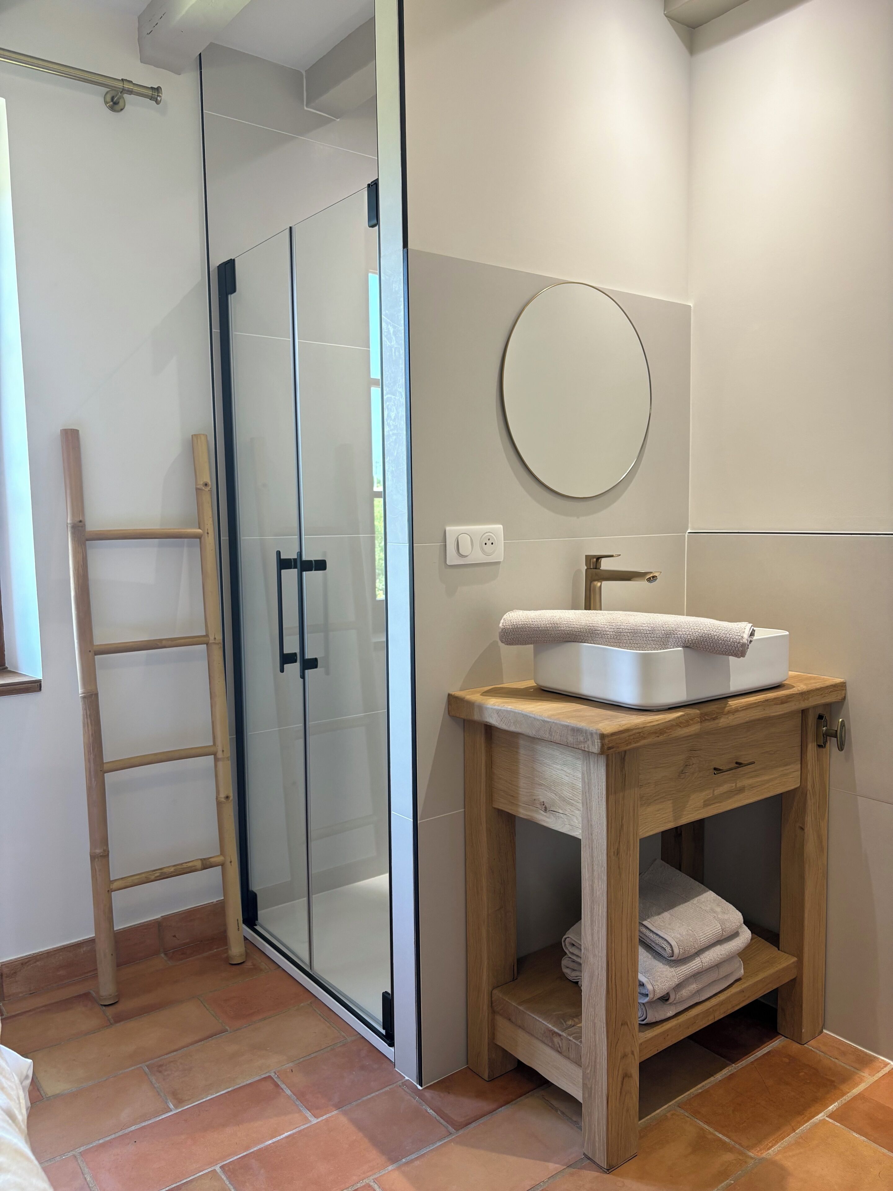 Un baño con cabina de ducha de vidrio, tocador de madera con lavamanos y un perchero para toallas.