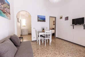Ein gemütlicher Wohnbereich mit Sofa, Esstisch mit Stühlen, einem an der Wand befestigten Fernseher und einer Küchenzeile im Hintergrund.