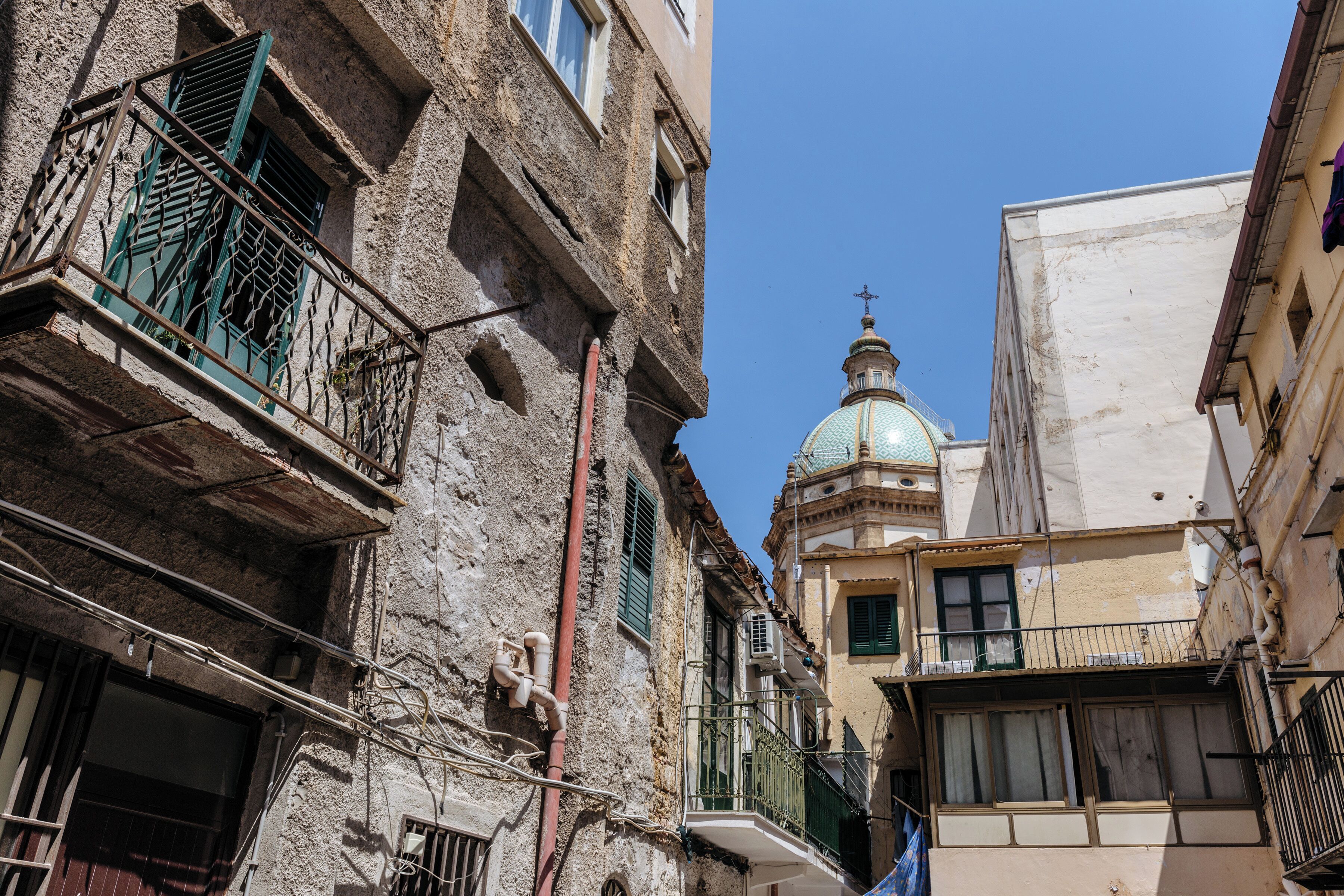 A narrow street with old buildings, a visible dome, and a cross on top of a building.
