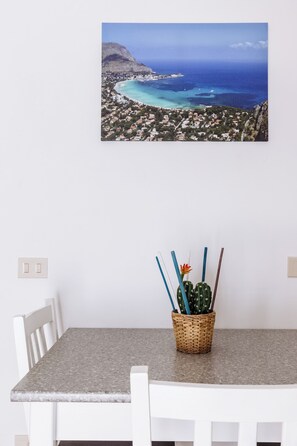 A dining area with a table, chairs, a wall-mounted picture of a coastal landscape, and a wicker basket with a cactus plant. - PILLY House Ballaró is located in a historic building at the entrance to the Ballaró Market (Palermo)