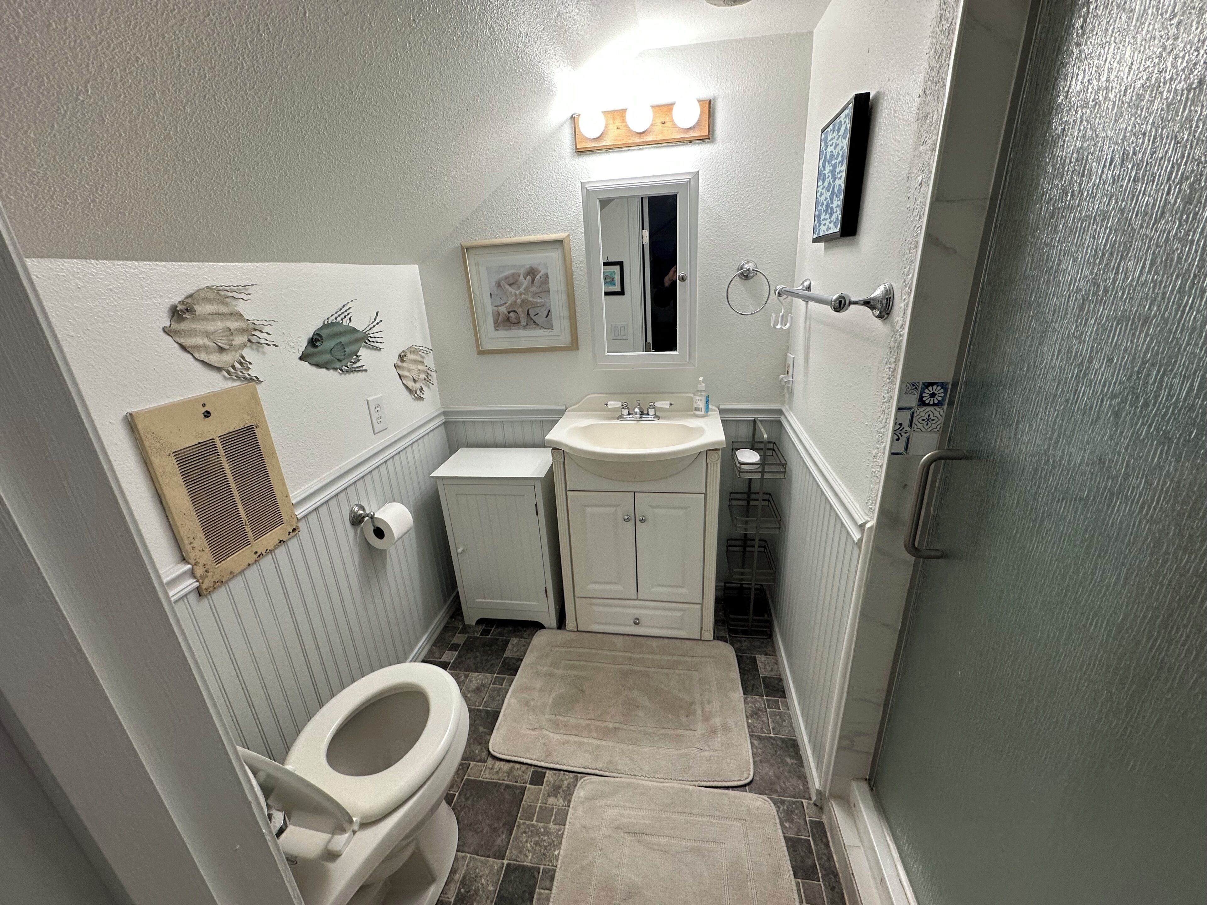 A small bathroom with a toilet, sink, vanity, and a shower area.