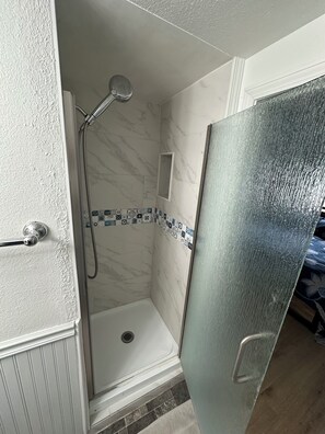 Eine Dusche mit Duschbrause, einer kleinen Ablage und einer gefliesten Wand mit blau-weißem Muster.
