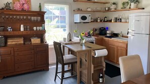 A kitchen with wooden cabinets, a dining table, chairs, a refrigerator, and various kitchen appliances. - Sit and relax a while (Natchez)