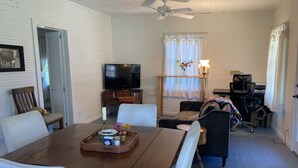 A dining area with a wooden table, white chairs, a television, and a window with curtains. - Sit and relax a while (Natchez)