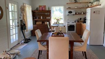 A dining area with a wooden table and chairs, a kitchen with appliances, and a window with curtains.
