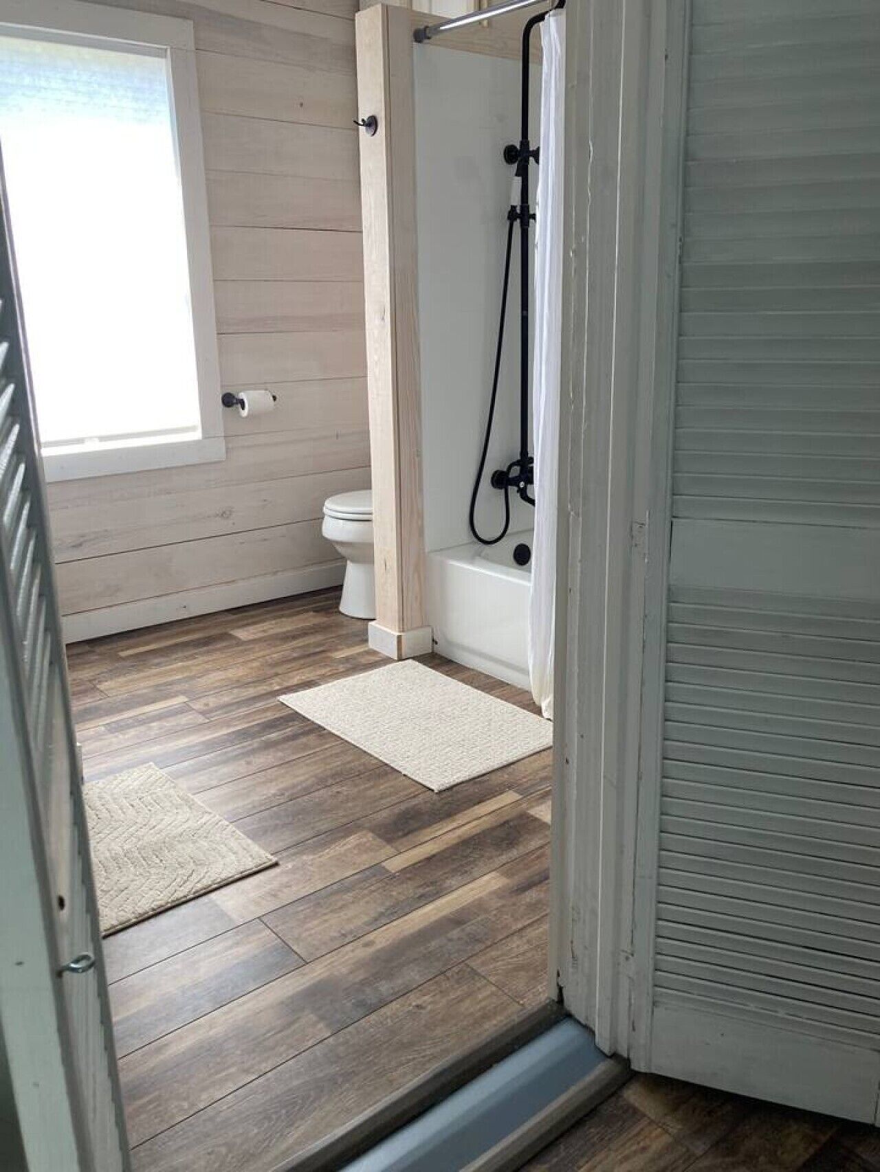 A bathroom with a shower, toilet, and a window.