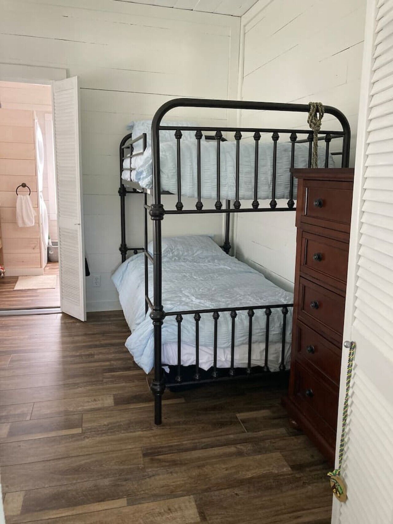 A bunk bed with a wooden dresser, a wooden floor, and a white door.