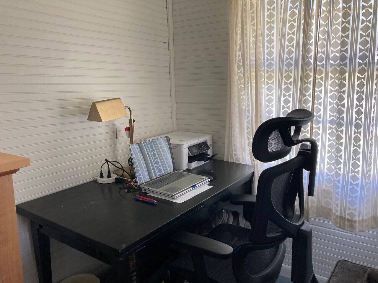 A room with a desk, a laptop, a printer, a lamp, and a chair.