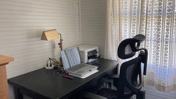 A room with a desk, a laptop, a printer, a lamp, and a chair.