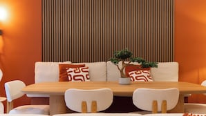 Een eetgedeelte met een houten tafel, witte stoelen en een bank met gekleurde kussens.