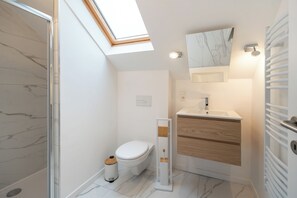 Ein modernes Badezimmer mit Dachfenster, Toilette, Waschbecken mit Marmorplatte und Holzschrank.