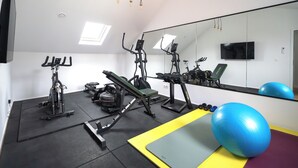 Een sportschool met fitnessapparatuur, een grote spiegel en een televisie aan de muur.