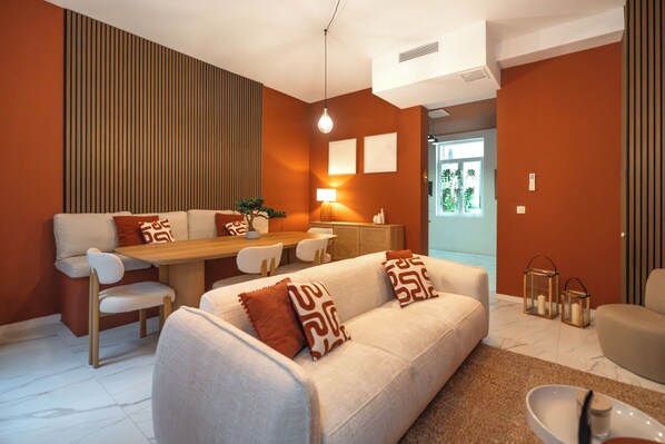 Un salon moderne comprenant un canapé, une table à manger et des chaises, une lampe, et donnant sur l’extérieur.