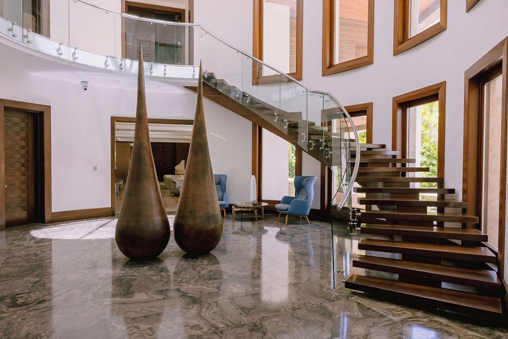 A spacious lobby with a modern staircase, large vases, and a polished marble floor.