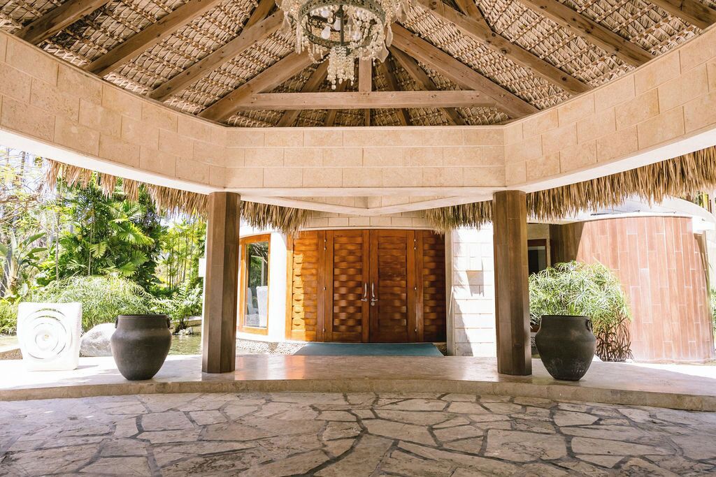 A covered outdoor area with a thatched roof, stone walls, and a wooden door.