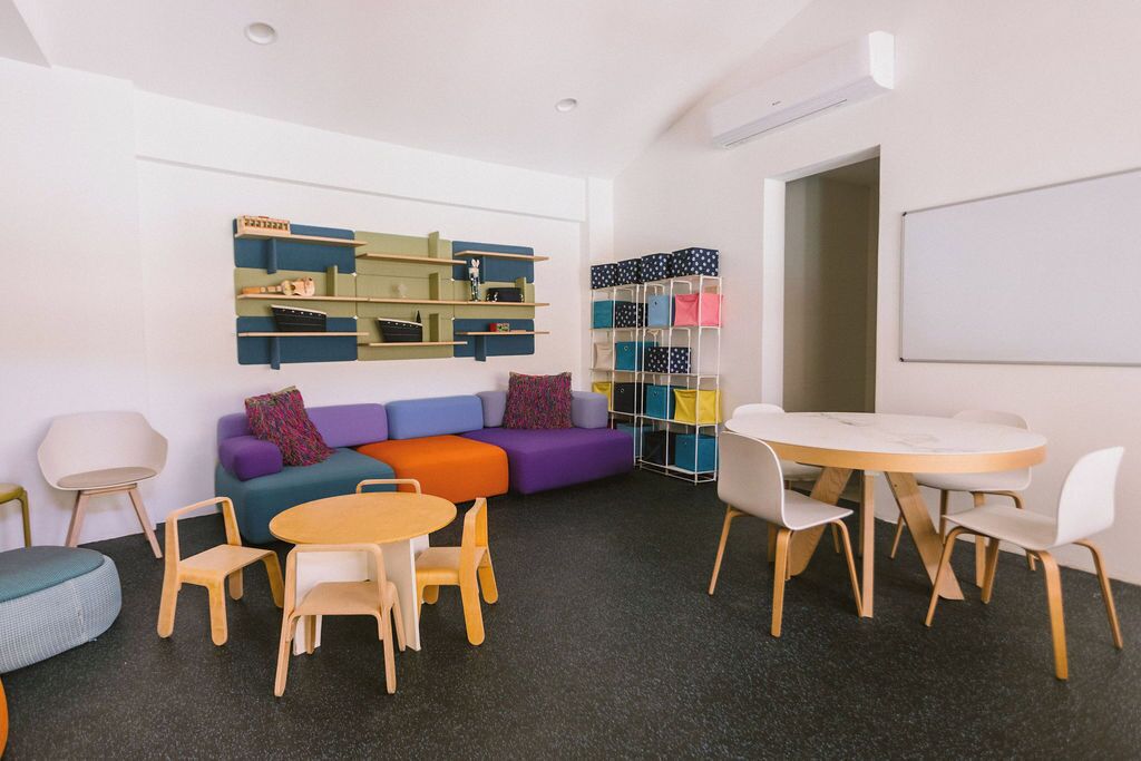 A room with a sofa, chairs, a table, and storage units.