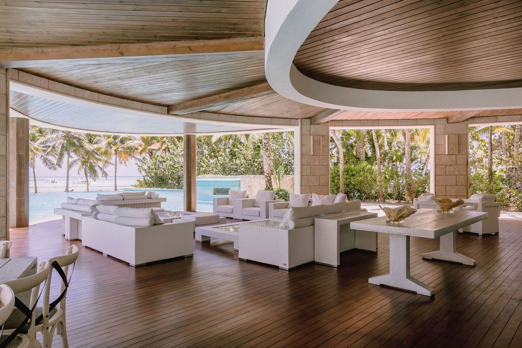 Un vaste espace de détente extérieur, avec des meubles blancs, une piscine et une vue sur l’océan.