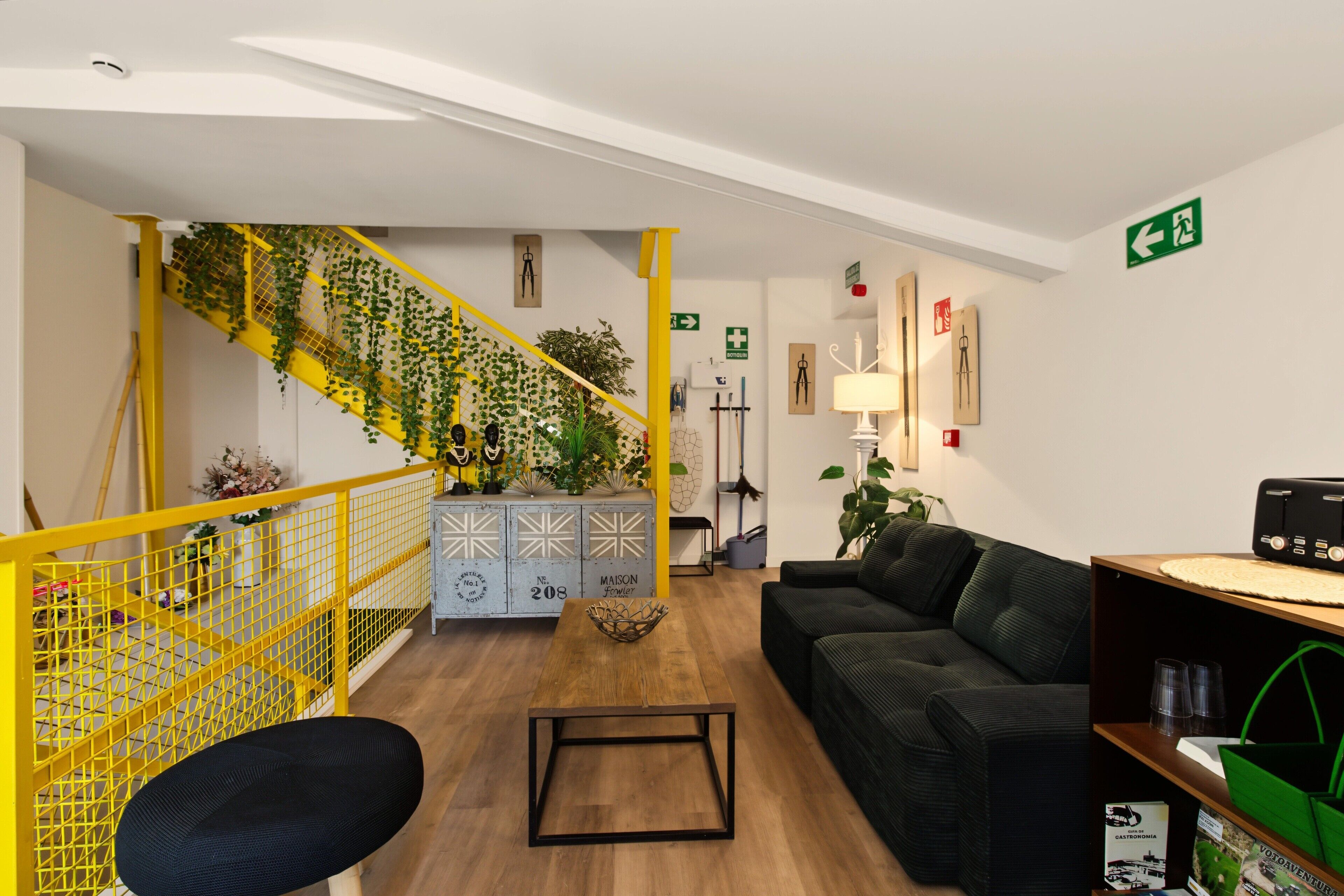 Un interior moderno con una escalera, un sofá negro, una mesa de centro de madera y una estantería.