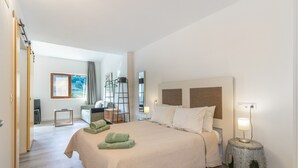 Habitación de hotel con cama, mesita de noche, lámpara y vistas al pasillo.