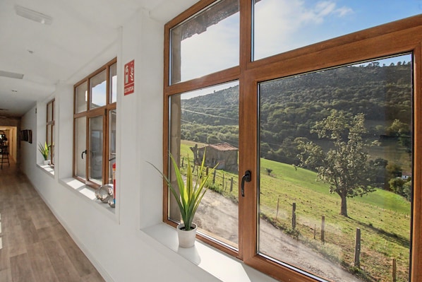A corridor with large windows offering a view of a rural landscape.