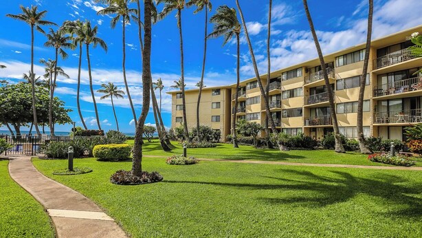 Un hotel con varios balcones, un césped cuidado y palmeras.